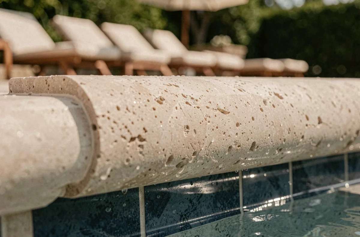 Gros plan sur une margelle en calcaire brossé avec profil arrondi en bord de piscine