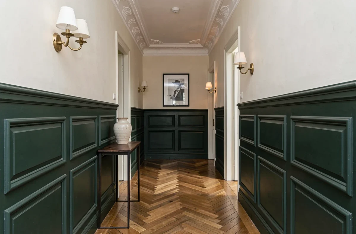Couloir haussmannien avec lambris vert foncé en demi-hauteur et parquet en chevrons, style classique parisien