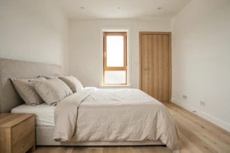 Chambre moderne avec lit double positionné face à la porte en bois, vue grand angle montrant l'axe lit-porte